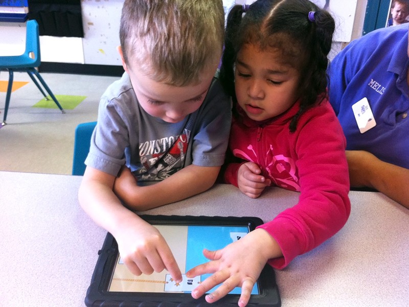 Two preschoolers playing a game on the same ipad. They're connecting two cards together.