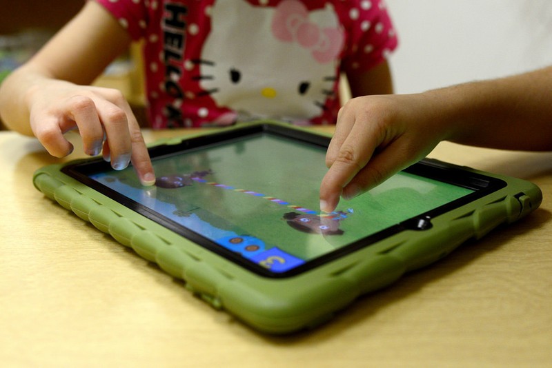 Two preschoolers' hands touching an iPad screen, playing the Treasure Bubbles game.