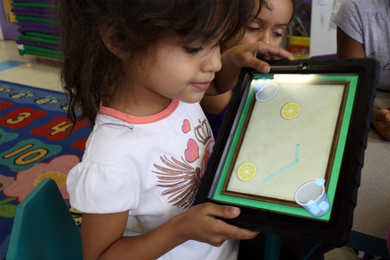 A preschool student playing Lemonade Stand and tilting the iPad.