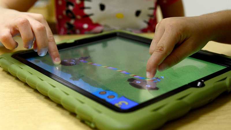 Two preschoolers’ hands touching an iPad screen, playing the Treasure Bubbles game.